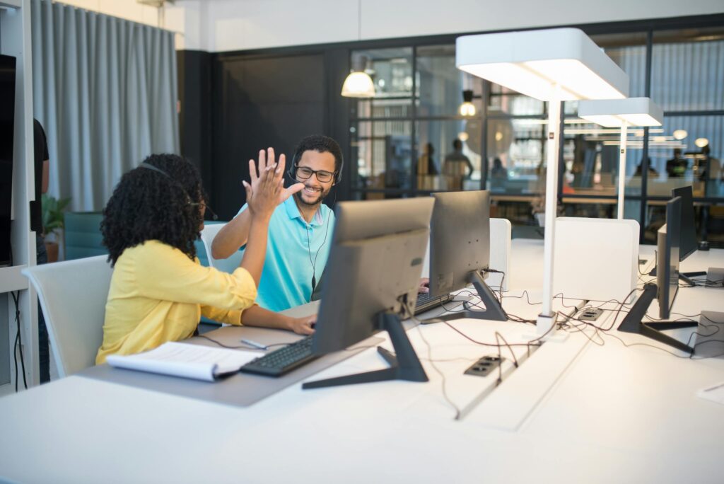 Two colleagues celebrate success with a high-five in a modern open-plan office environment.